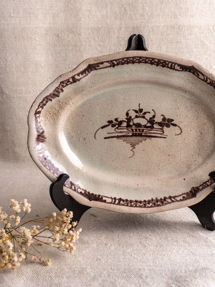 Antique French Cul Noir faience platter with manganese decorative border on a dark stand and textured beige fabric with dried flowers.