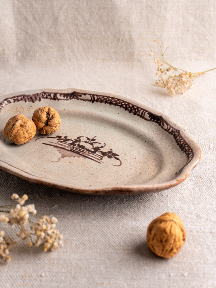 Antique French Cul Noir faience platter with brown pattern, displayed with three walnuts on beige textured fabric and dried white flowers.