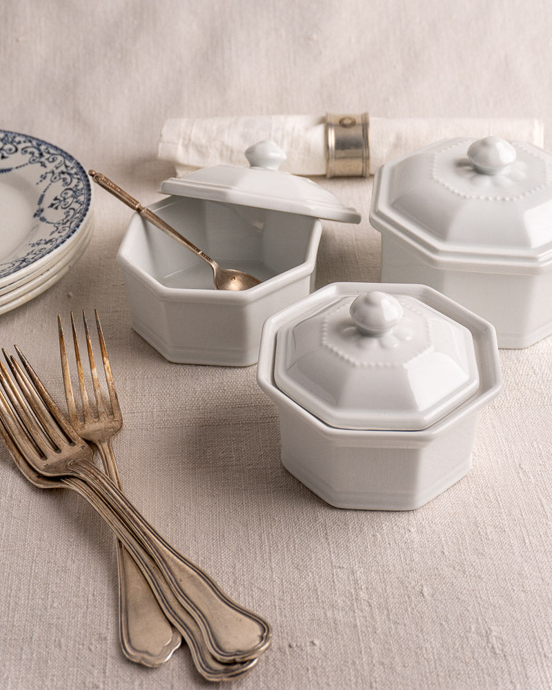 Set of three white octagonal Apilco porcelain pots with lids, on neutral fabric background.