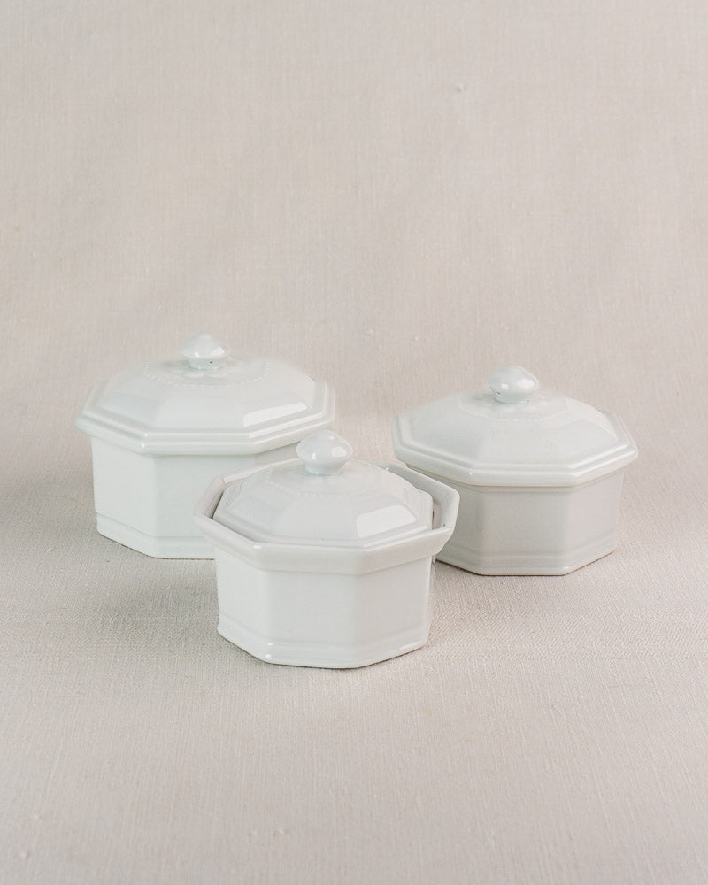 Set of three white octagonal Apilco porcelain pots with lids, on neutral fabric background.