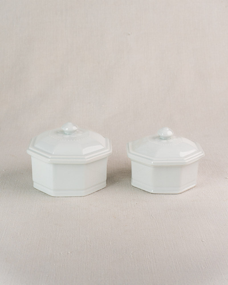 Set of three hexagonal white Apilco Modèle de José vintage French porcelain pots with lids on beige surface.
