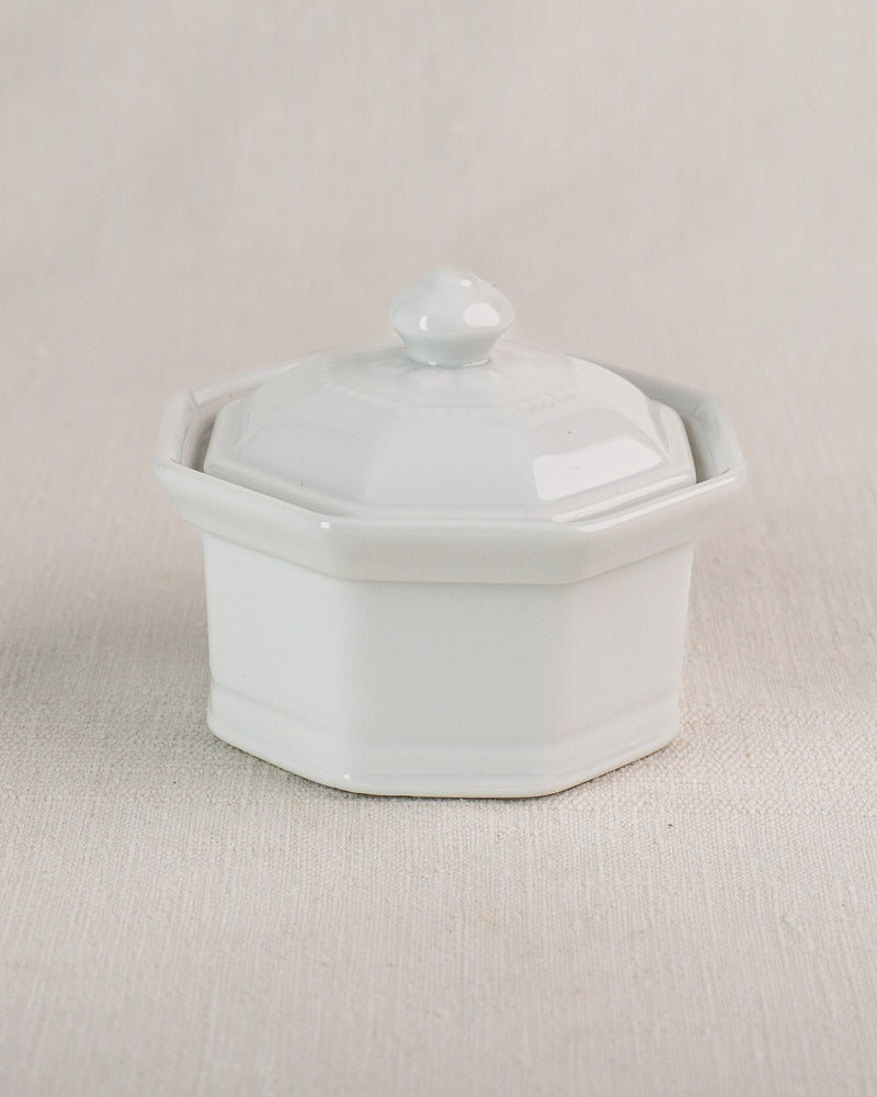Small white hexagonal Apilco porcelain pot with lid, Vintage French "Modèle de José" set, on beige surface.
