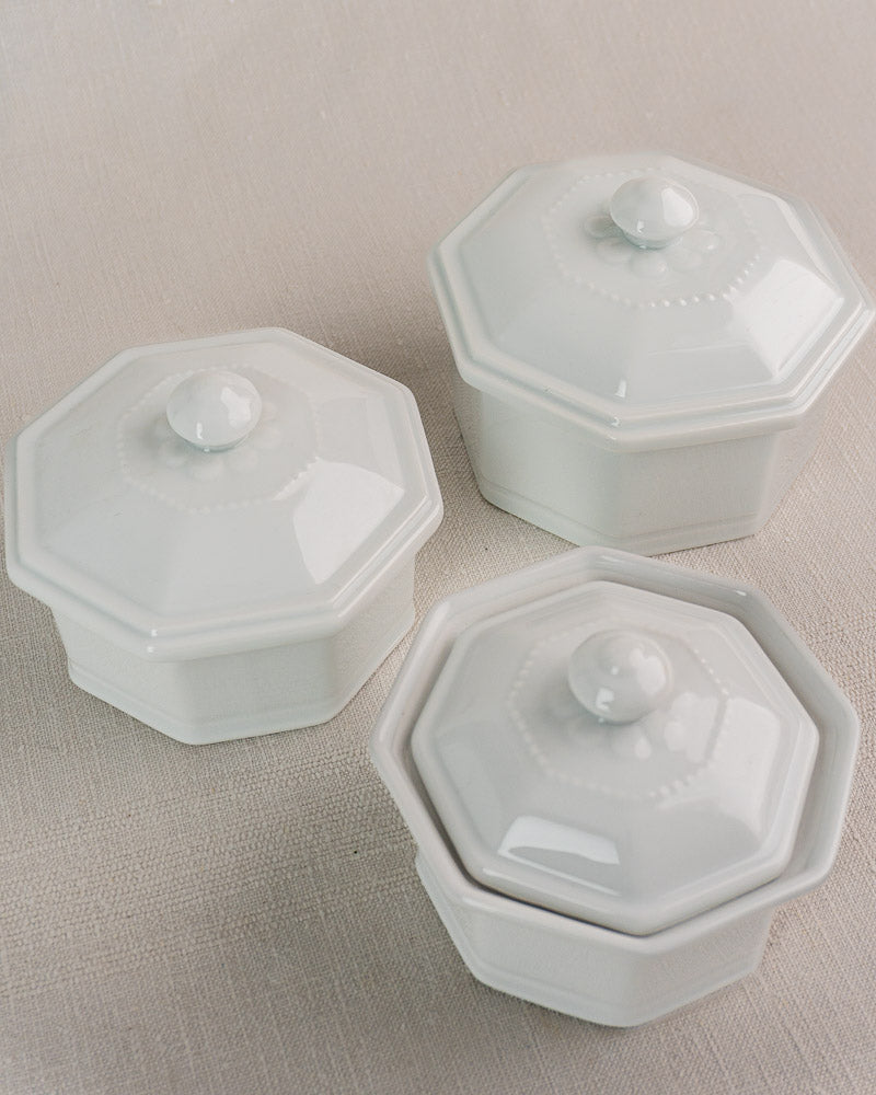 Set of three white octagonal French Apilco porcelain pots with matching lids on beige surface.