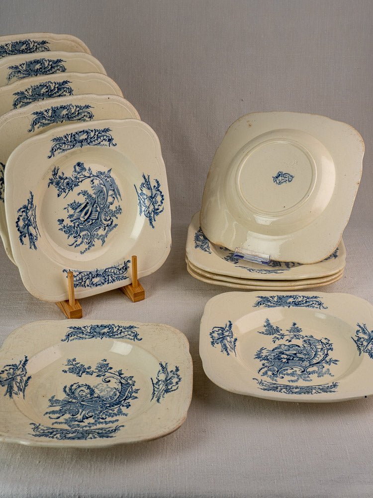 Antique French Clairefontaine faience plates with blue floral motifs, stacked on a wooden stand.