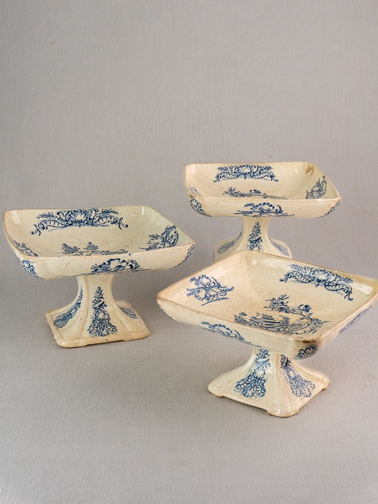 Antique French Clairefontaine faience dishes with blue floral designs on cream, on gray surface.