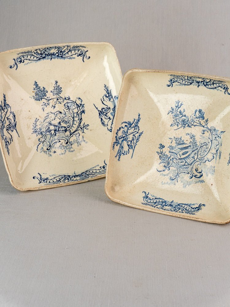 Vintage square ceramic plates with ornate blue transferware floral and landscape motifs on gray background.