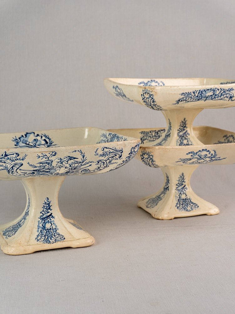 Stacked antique French faience compotes with square bases and detailed blue floral Clairefontaine designs.
