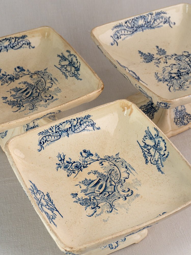Three vintage French ceramic pedestal dishes with blue floral patterns and aged patina on neutral surface.