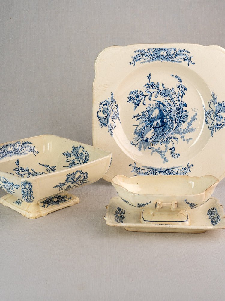 Four vintage cream ceramic faience pieces with blue pastoral motifs from the Clairefontaine Louis XV Terre de Fer set against a light gray background.