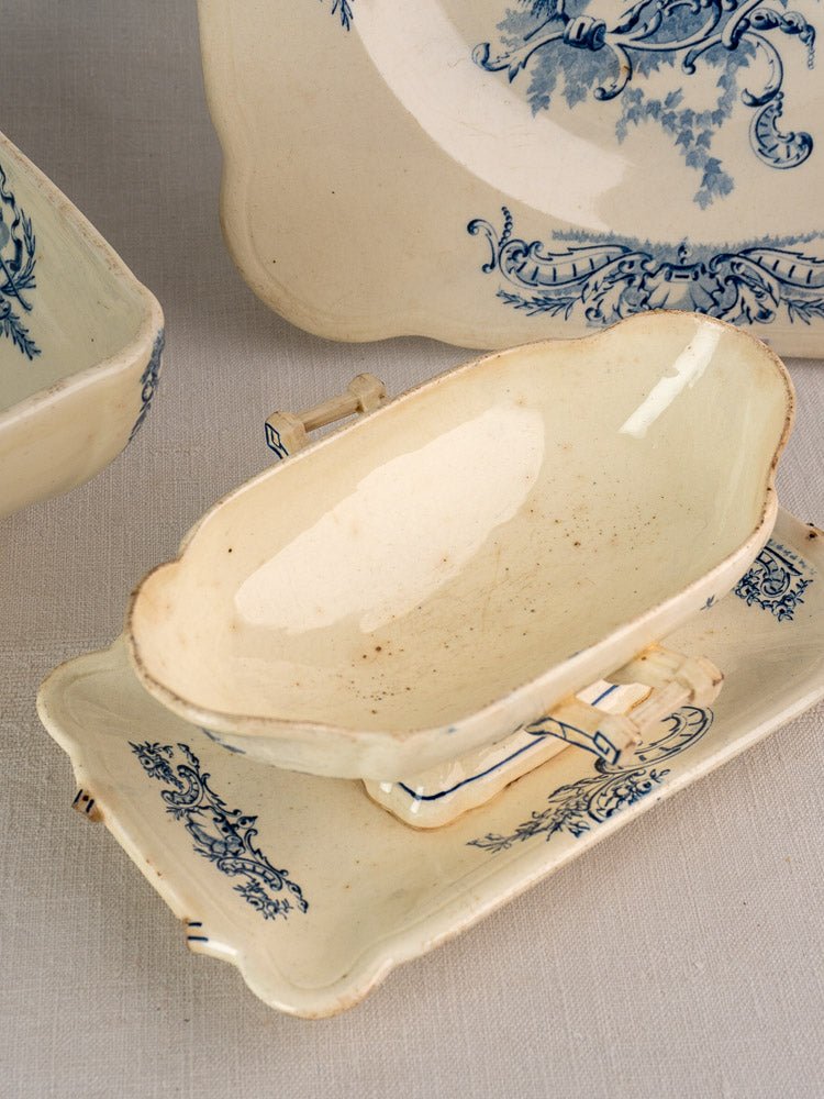 Cream porcelain gravy boat and tray with blue floral motifs from Clairefontaine faience service, on beige cloth.