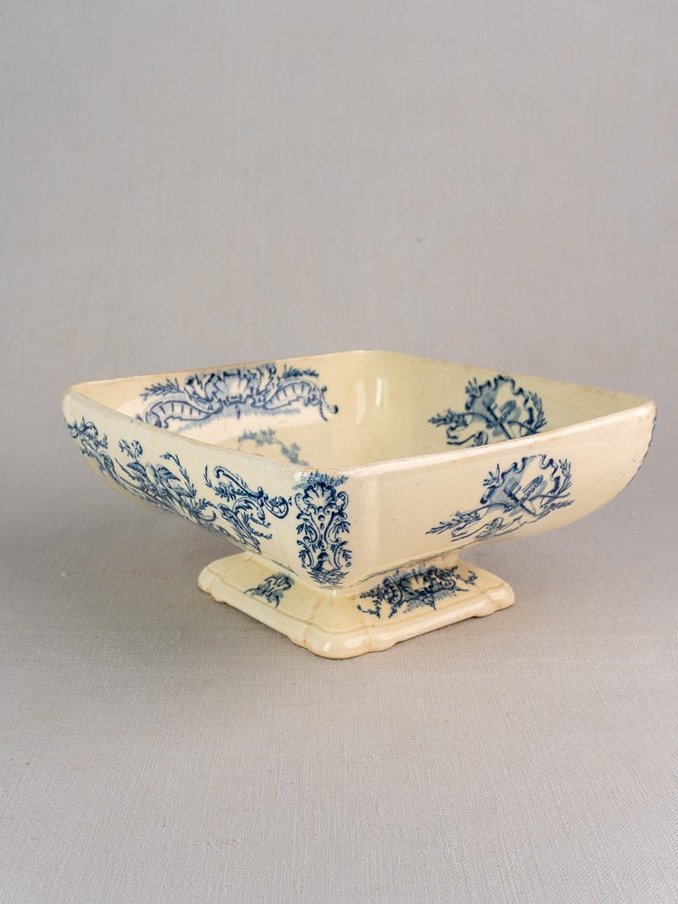 Cream ceramic square bowl with blue floral pattern and pedestal base, Clairefontaine faience style.