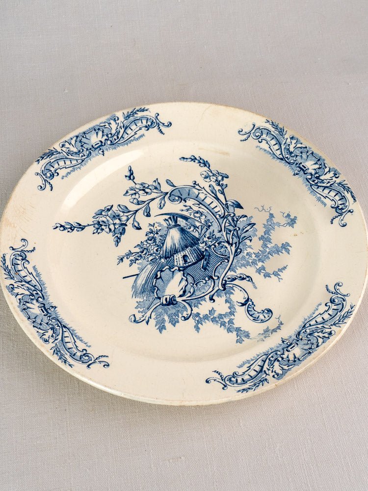 Cream-colored Clairefontaine faience plate with blue floral rim and central hut motif, Louis XV Terre de Fer.