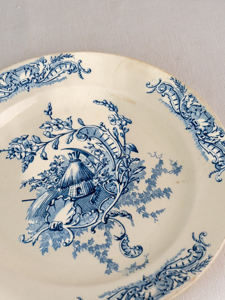 Antique French Clairefontaine faience plate with blue floral motifs and tepee on cream, on fabric.