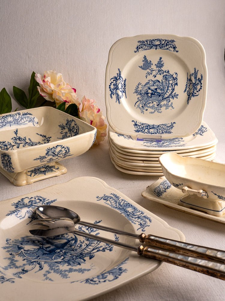 Antique French Clairefontaine faience dinnerware set with blue floral motifs, arranged beside pink flowers.