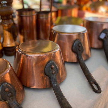 Vintage French copper saucepans with iron handles arranged on a market table, warm patina catching soft natural light