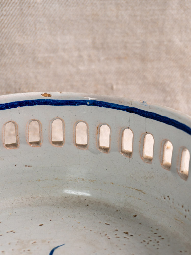 Antique French faience jardinière with cobalt blue rim, rectangular cutouts, chipped white ceramic on beige fabric.