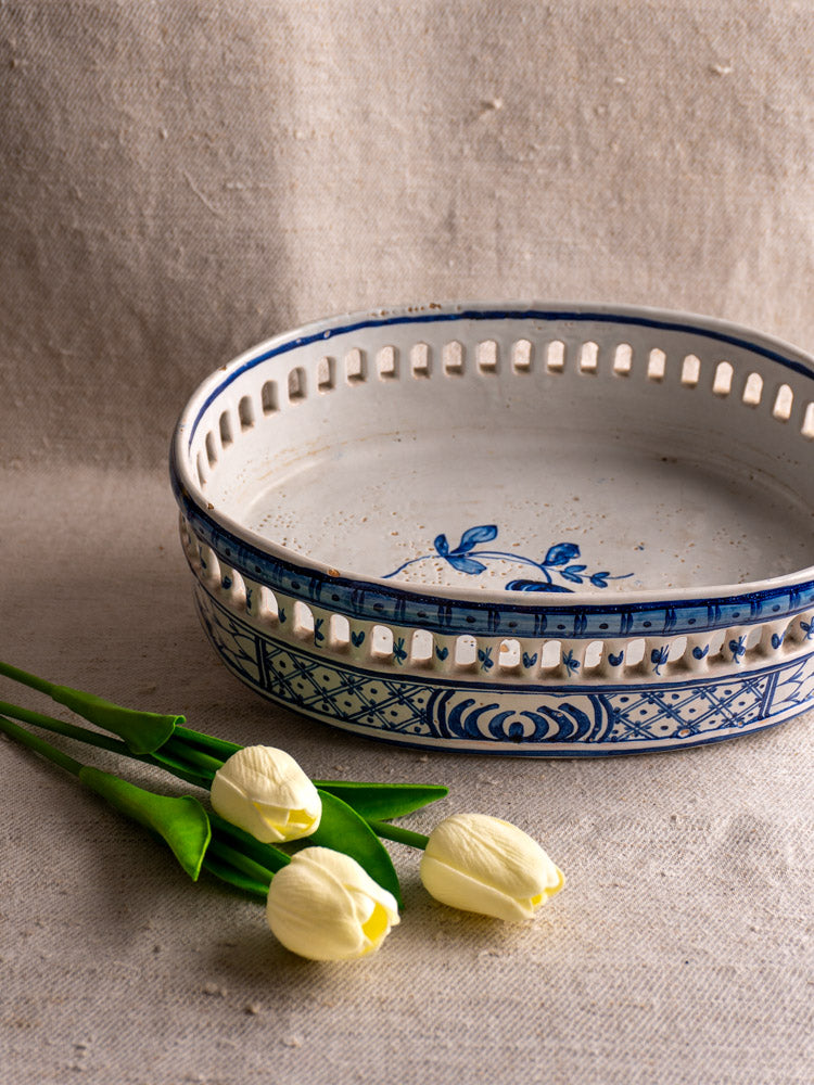 Antique French faience jardinière by Pouplard Béatrix with cobalt blue glaze beside pale yellow tulips on beige fabric.