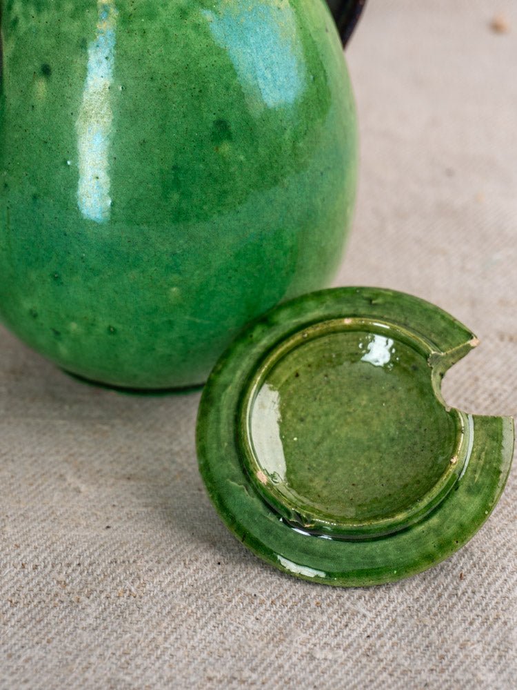 Antique French Dieulefit green earthenware olive pot and matching ashtray with rim chip on beige textured fabric.