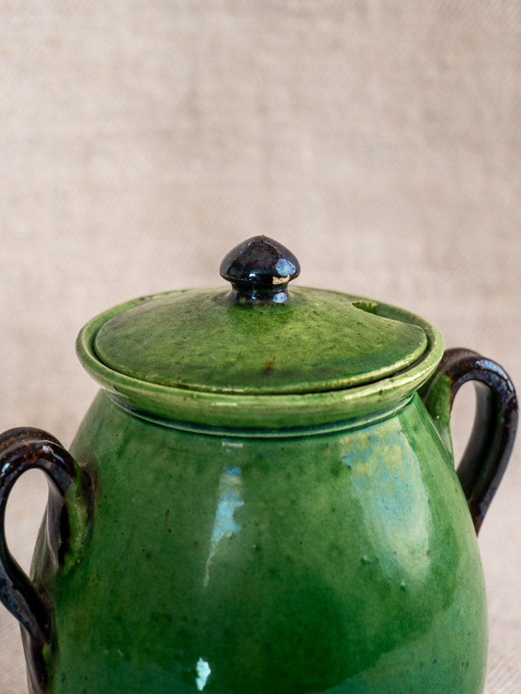 Antique French Dieulefit green earthenware olive pot with matching lid and two dark handles on neutral background.