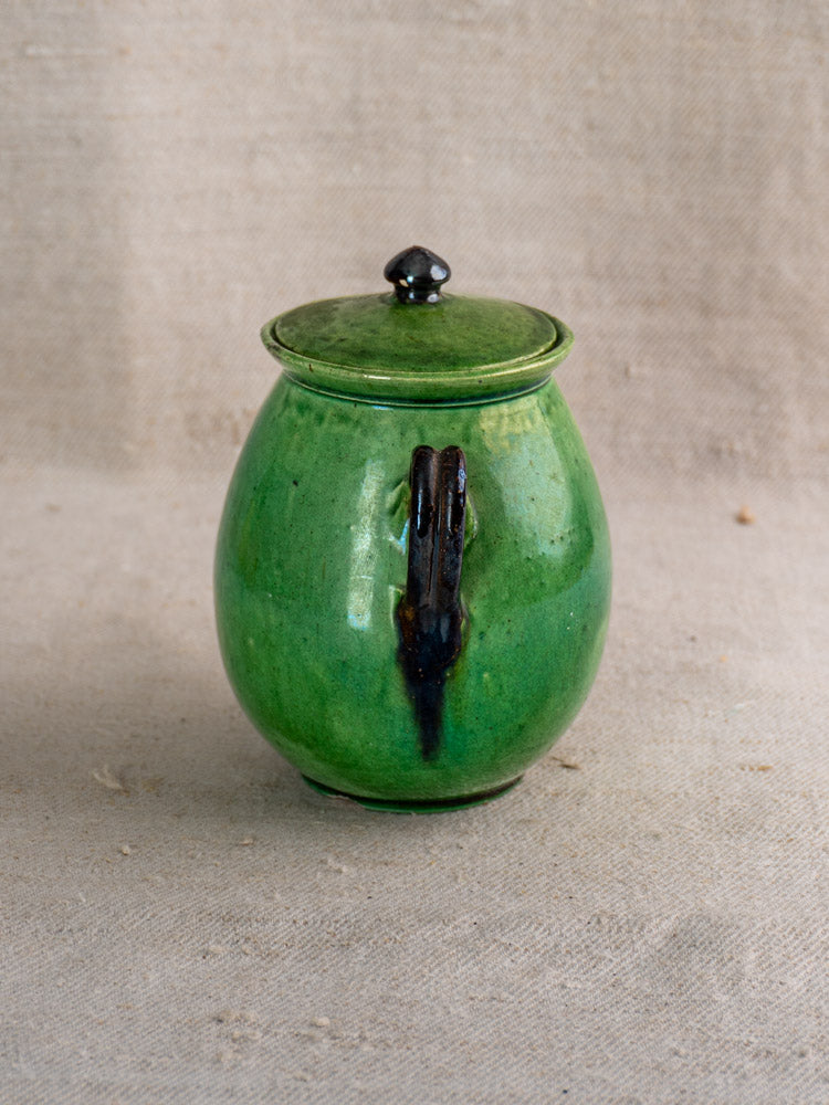 Early 20th-century French olive pot in Dieulefit green earthenware with lid and handle on beige fabric.