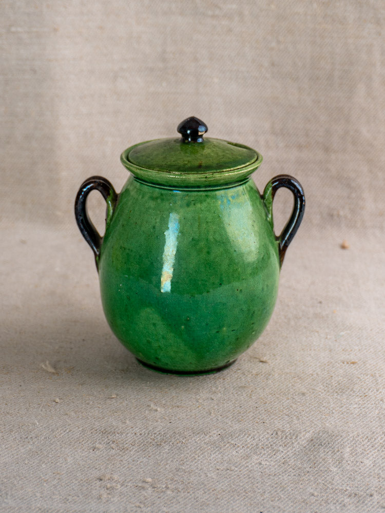 Early 20th century French Dieulefit green earthenware olive pot with two handles and lid on beige textured fabric.