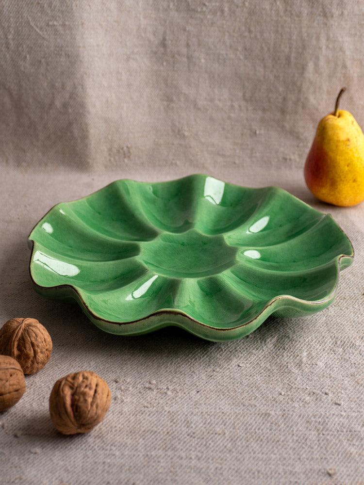 Pair of mid-century Dieulefit French ceramic melon dishes with green scalloped design, on beige cloth beside fruit and walnuts.