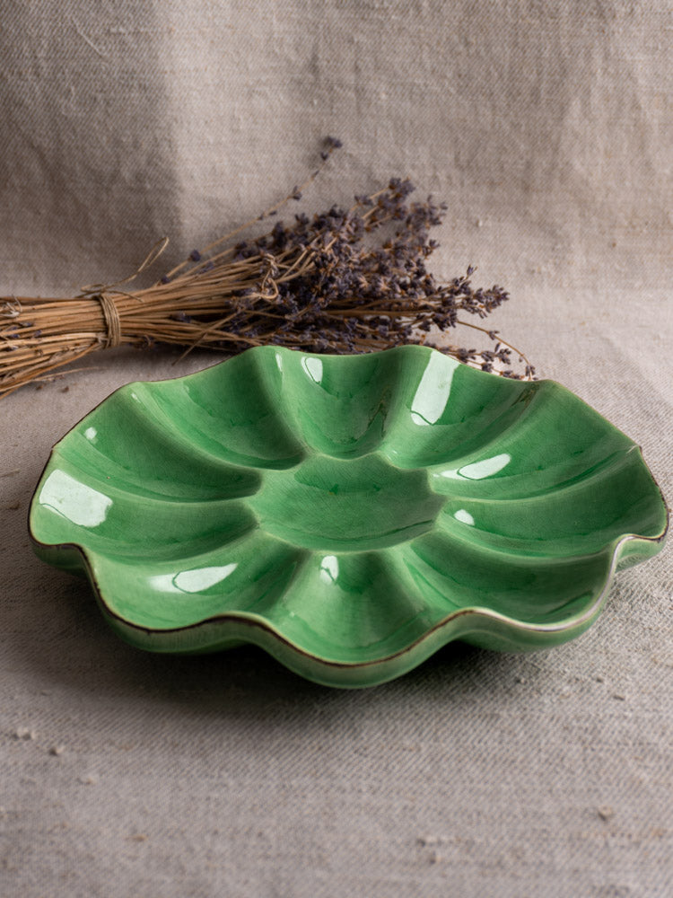 Antique French Dieulefit ceramic melon dish with emerald green glaze, on beige fabric with dried lavender nearby.