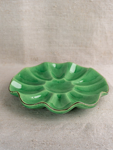 Antique French Dieulefit ceramic melon dish with emerald green glaze and scalloped edge on textured fabric background.