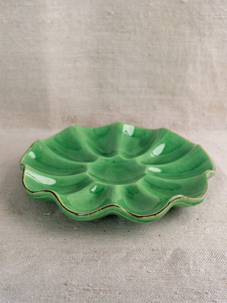 Antique French Dieulefit ceramic melon dish in emerald green glaze with scalloped, petal-like edges on beige textured fabric.