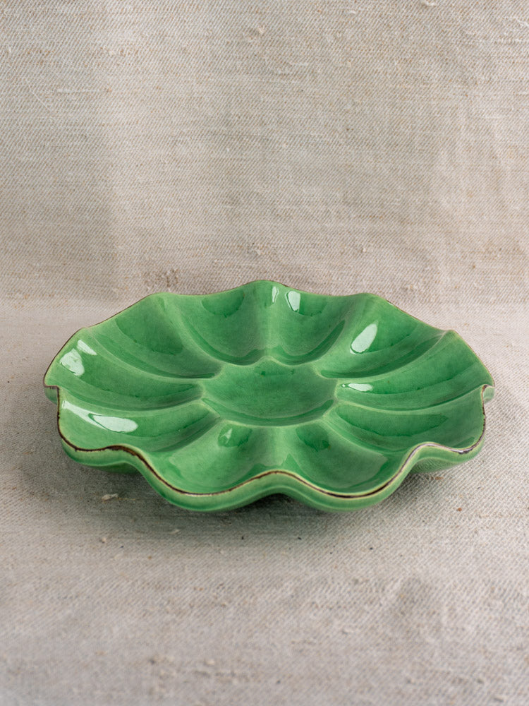 Antique French Dieulefit ceramic melon dish, emerald green glazed, scalloped edge, on light textured fabric.
