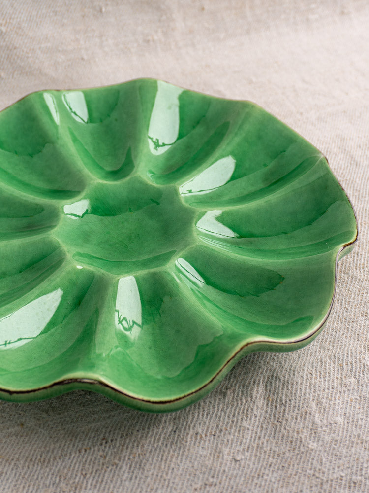 Antique French Dieulefit ceramic melon dish with emerald green glaze and scalloped edges on textured beige fabric.