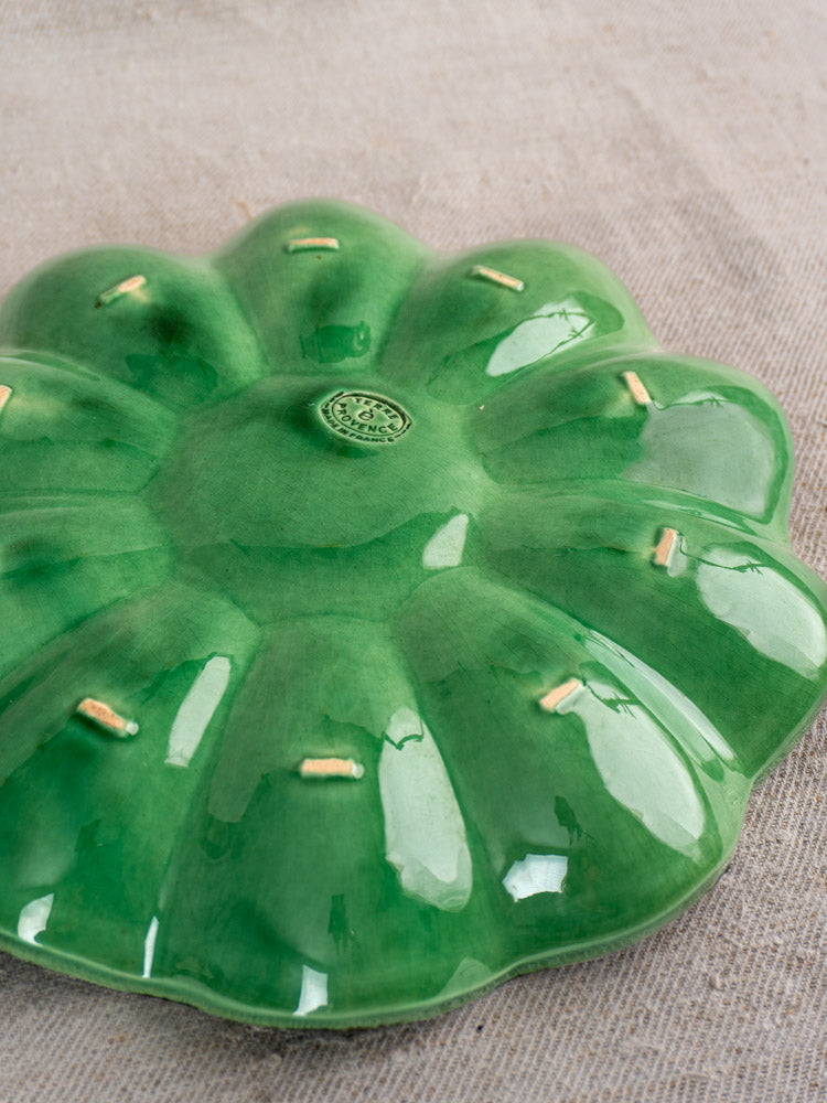 Antique French ceramic melon dish from Dieulefit, emerald green with eight petals, beige dots, on textured neutral surface.