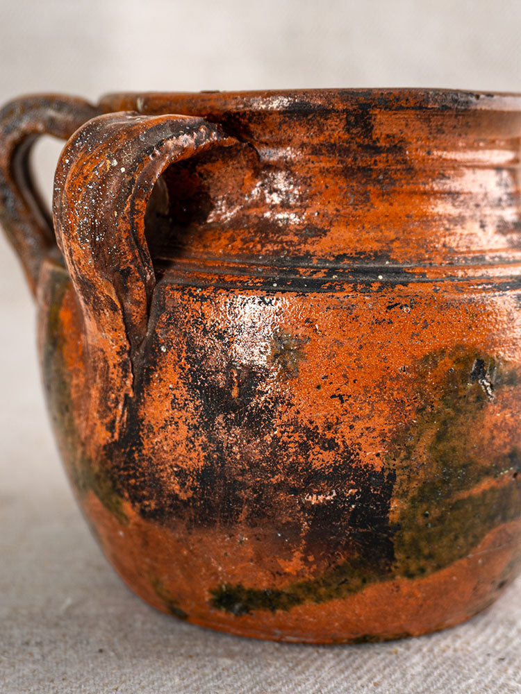 Antique French rillettes pot in glazed earthenware with tigré drip glaze, two handles, weathered finish, neutral background.