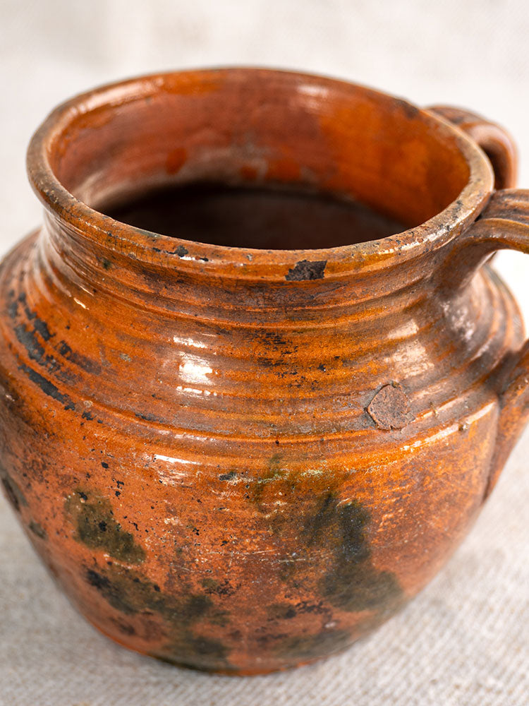 Antique French earthenware rillettes pot with Tigré drip glaze, two handles, blackened patina on beige textured surface.