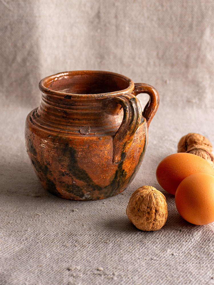 Antique French earthenware rillettes pot with brown Tigré drip glaze, round body, two handles, on textured fabric.