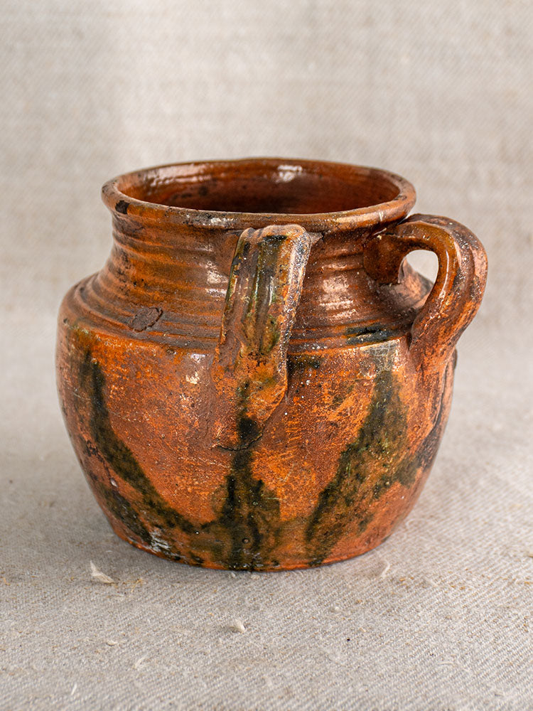 Antique French earthenware rillettes pot with brown Tigré drip glaze, round body, two handles, on textured fabric.