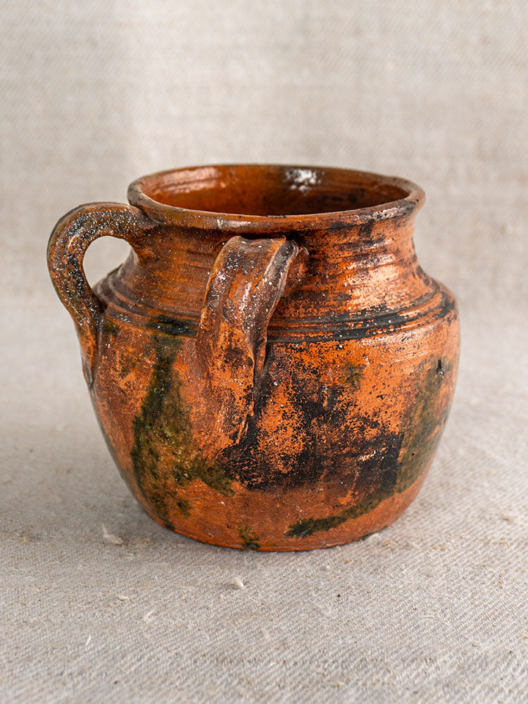 Antique French glazed earthenware rillettes pot with tigré drip glaze and single handle on beige textured fabric.