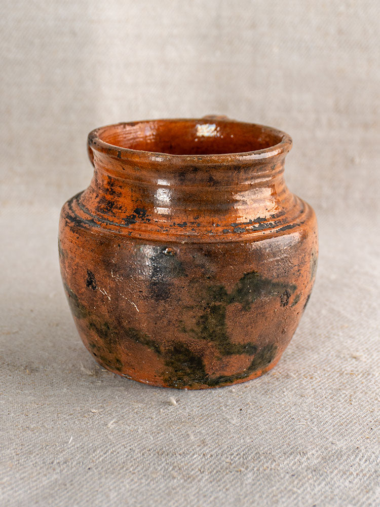 Antique French rillettes pot with earthy orange-brown tigré drip glaze, glazed earthenware on beige textured fabric.