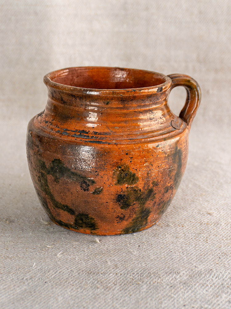 Antique French rillettes pot in glazed earthenware with Tigré drip glaze and single handle on beige fabric background.