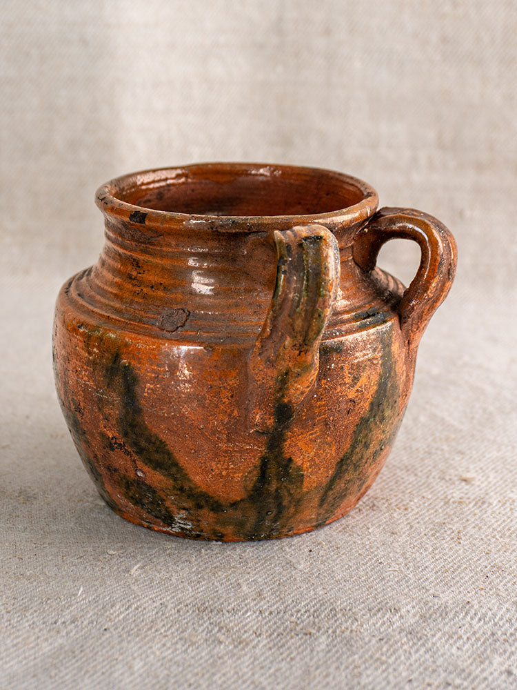 Antique French glazed earthenware rillettes pot with Tigré drip glaze, two handles, on woven fabric background.