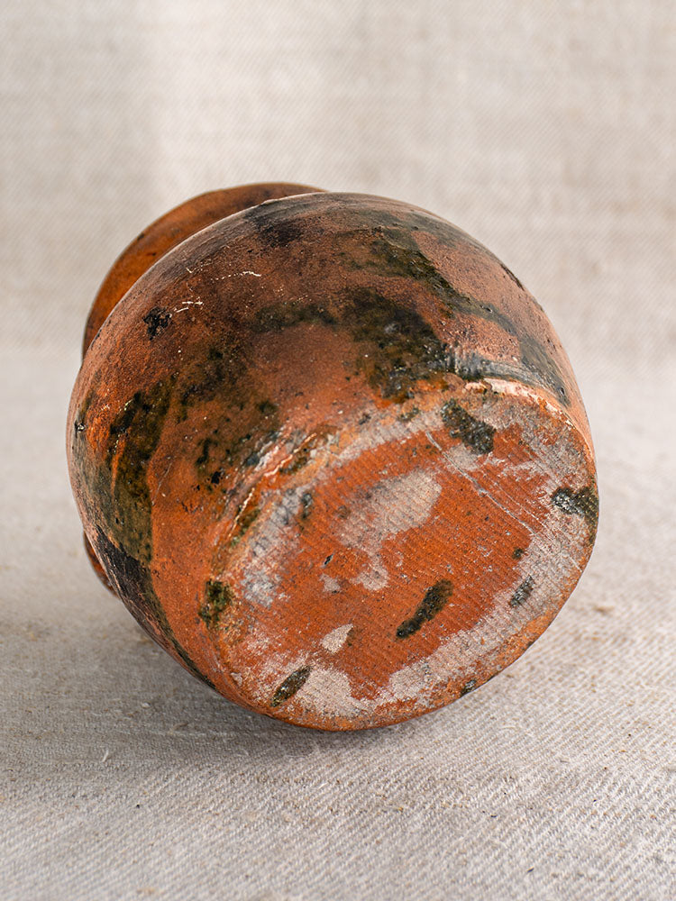 Antique French earthenware rillettes pot with Tigré drip glaze, round bottom, green accents, on pale fabric.