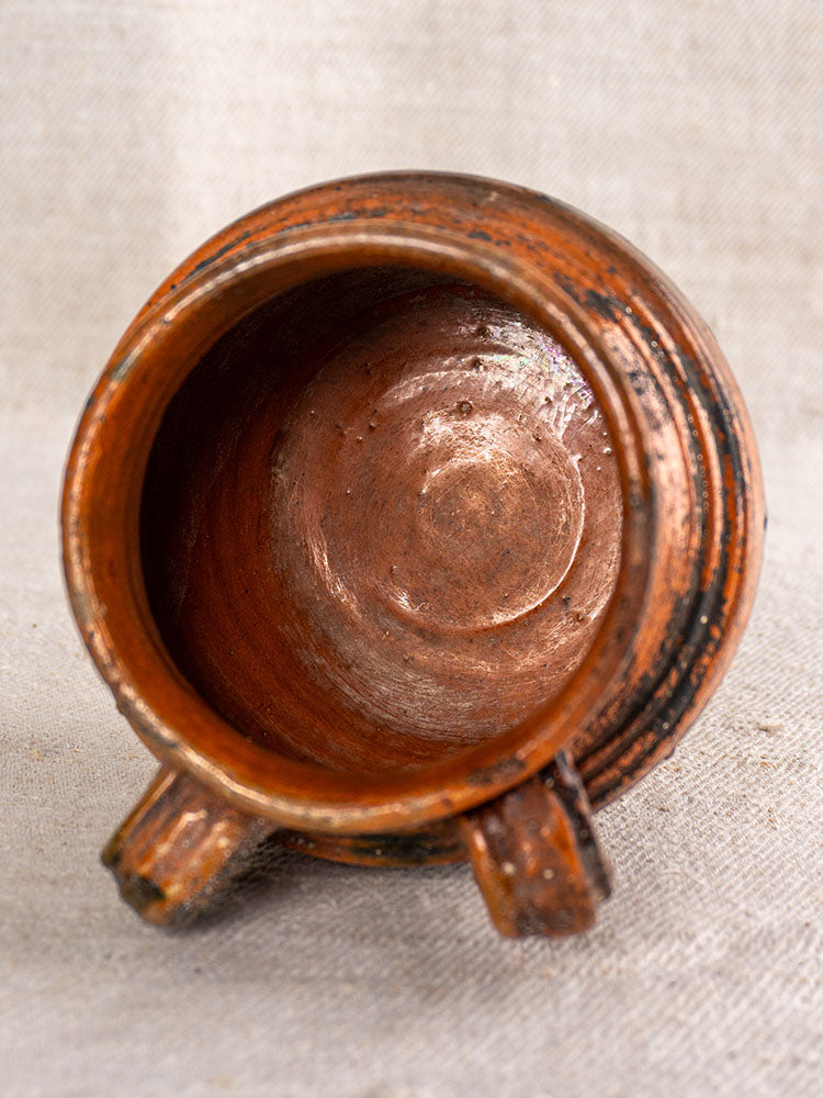 Antique French rillettes pot in glazed earthenware with Tigré drip glaze, viewed from above on light textured fabric.
