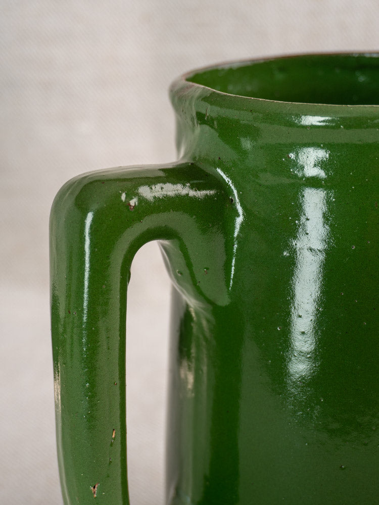 Antique French emerald green earthenware pitcher, early to mid 20th century, handle and rim shown on beige textured background.