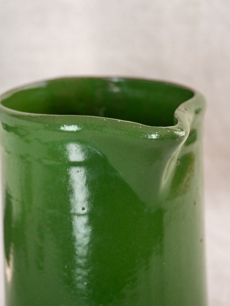 Antique French emerald green glazed earthenware pitcher with small spout, set on a neutral textured background.