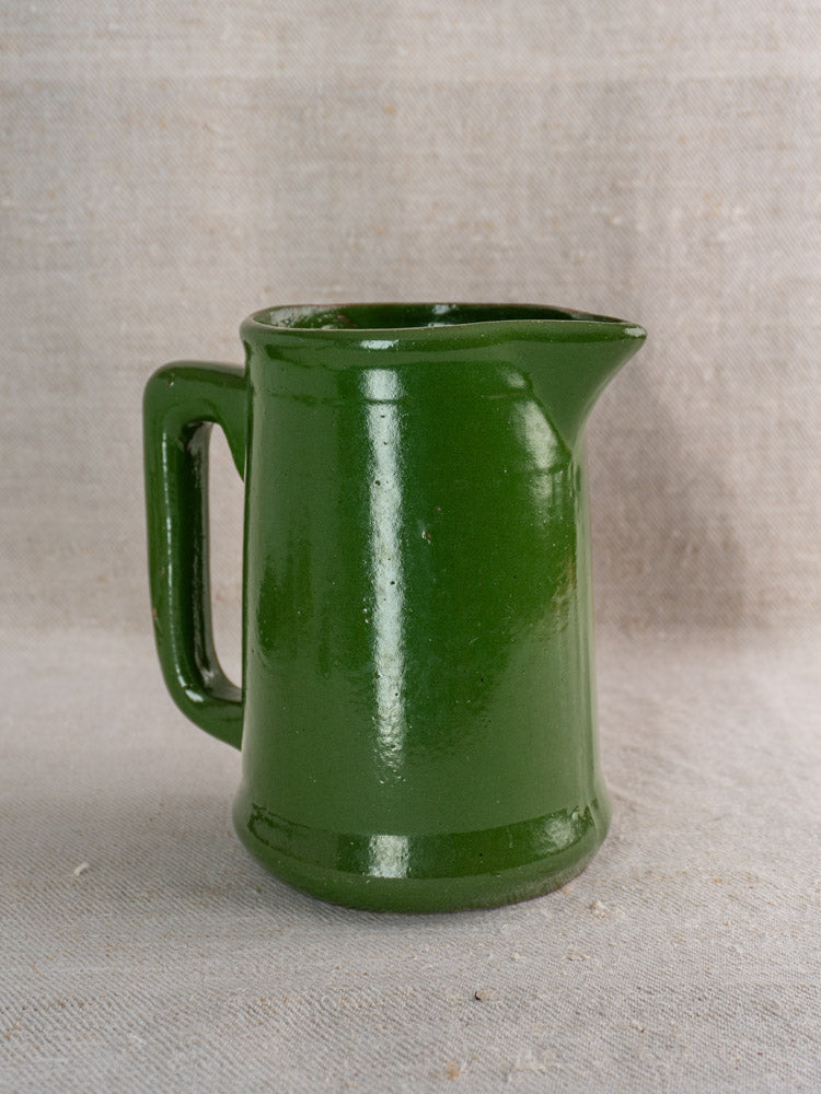 Antique French emerald green glazed earthenware pitcher with handle, shown on beige fabric with a neutral background.
