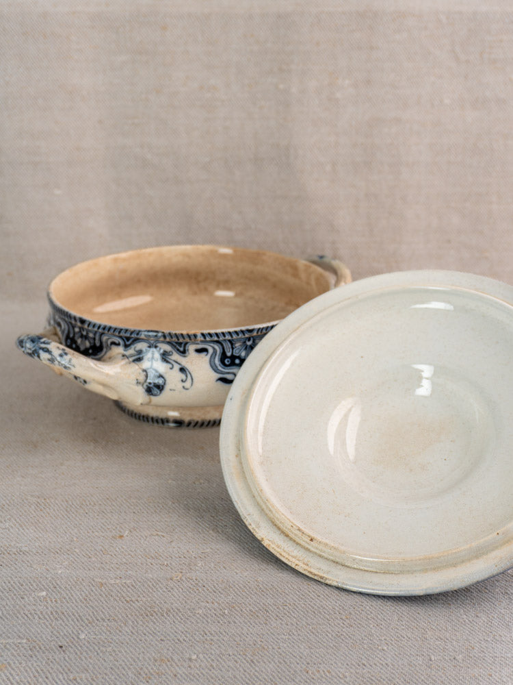 Antique French Badonviller Étoile serving dish with blue floral motifs and handles, matching lid beside, on beige fabric.