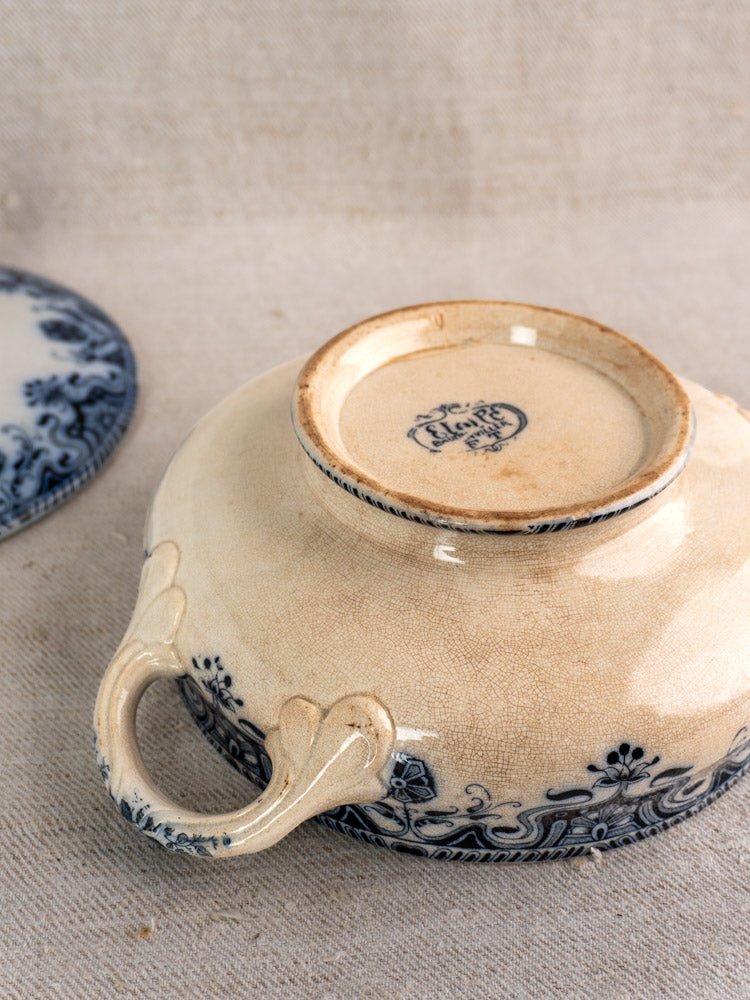 Antique French Badonviller Étoile covered serving dish upside down, blue floral design, maker’s mark visible on beige fabric.