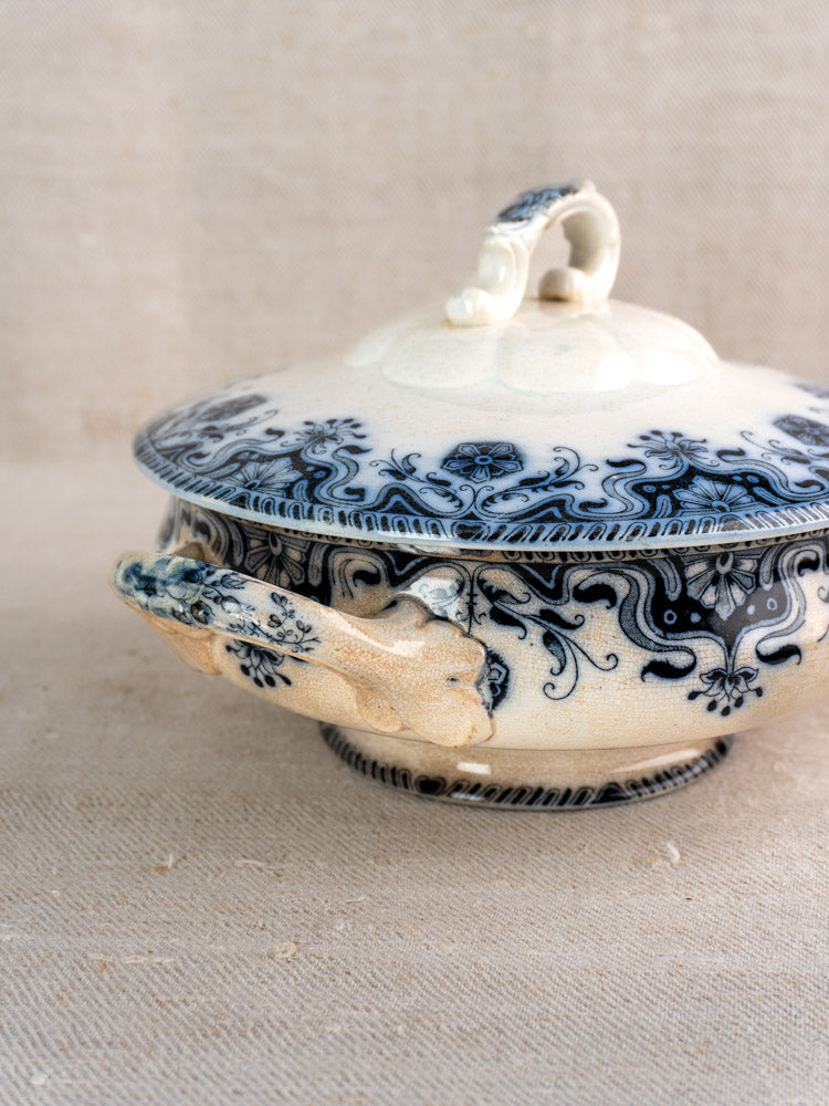 Antique French Badonviller Étoile covered serving dish, blue floral pattern, chipped handle, on beige textured surface.