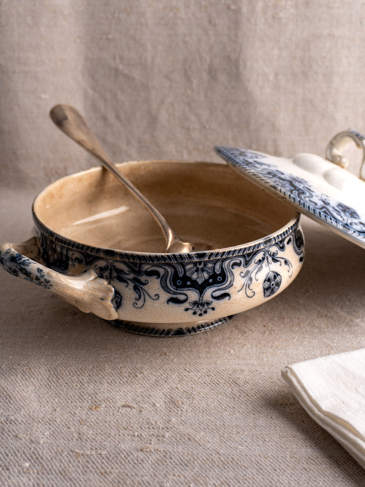 Antique French Badonviller Étoile covered serving dish with blue floral pattern and lid, metal ladle, on beige fabric.