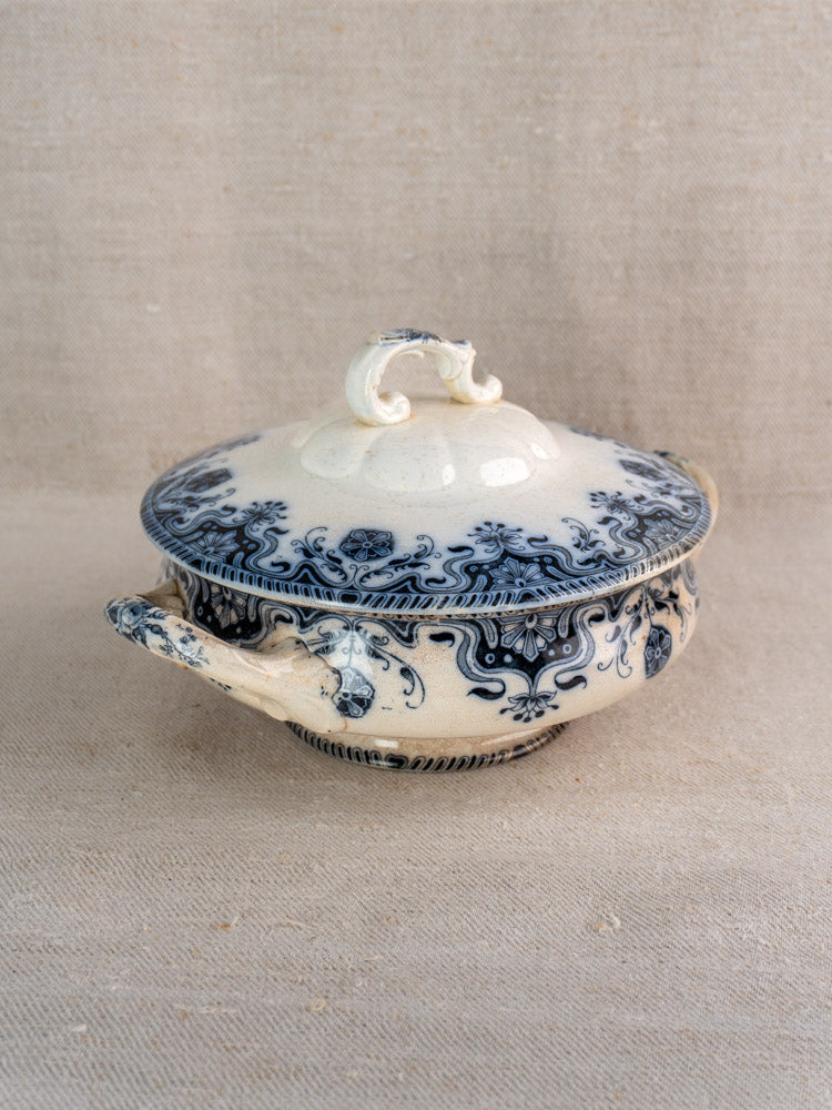 Antique Badonviller Étoile French ceramic soup tureen with ornate handles, sculpted lid, and blue floral motif on beige fabric.